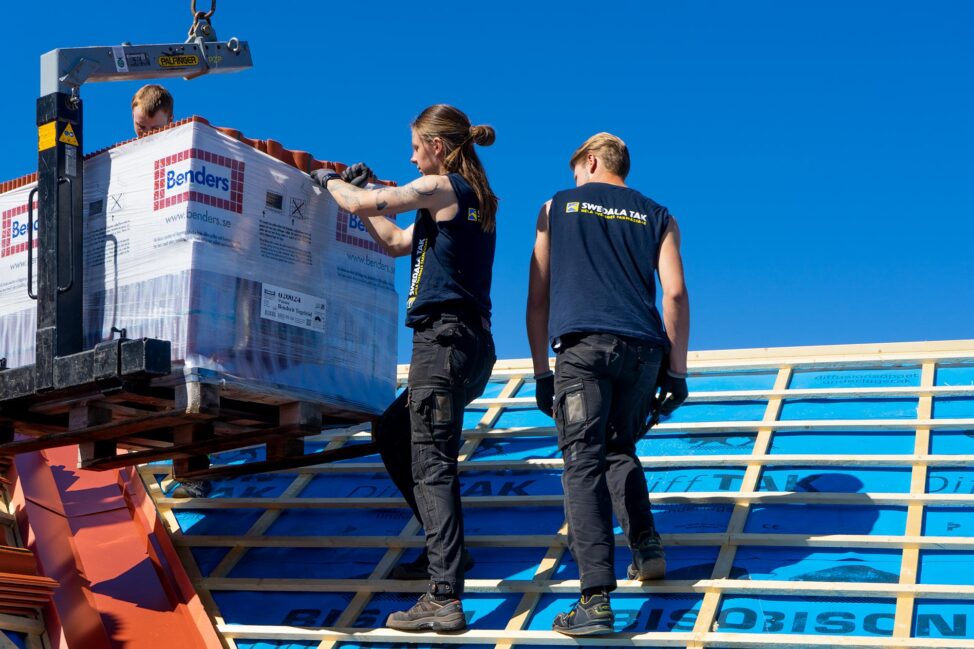 Två takläggare lastar av takpannor på ett tak i Borlänge