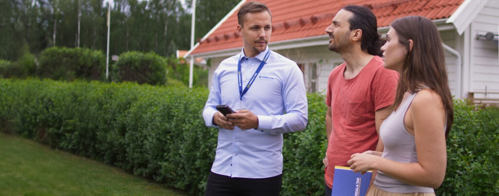 En takmästare pratar med två husägare utomhus inför ett takbyte.