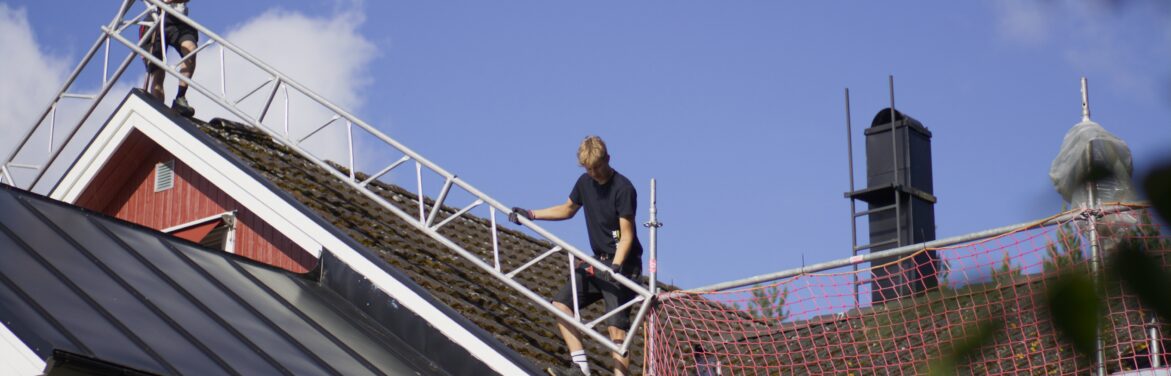 Takbyte som pågår på ett tak. Flera takbytare står uppe på det, fotografiet är taget snedd nedifrån.