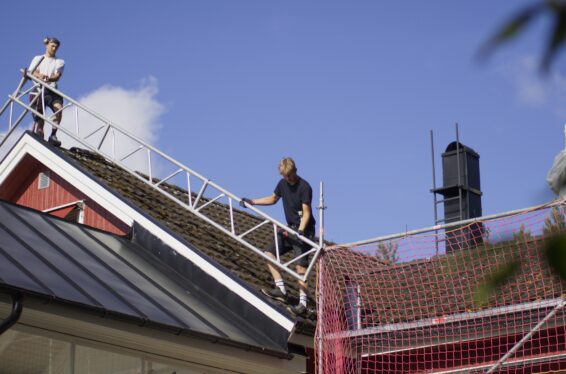 Takbyte som pågår på ett tak. Flera takbytare står uppe på det, fotografiet är taget snedd nedifrån.