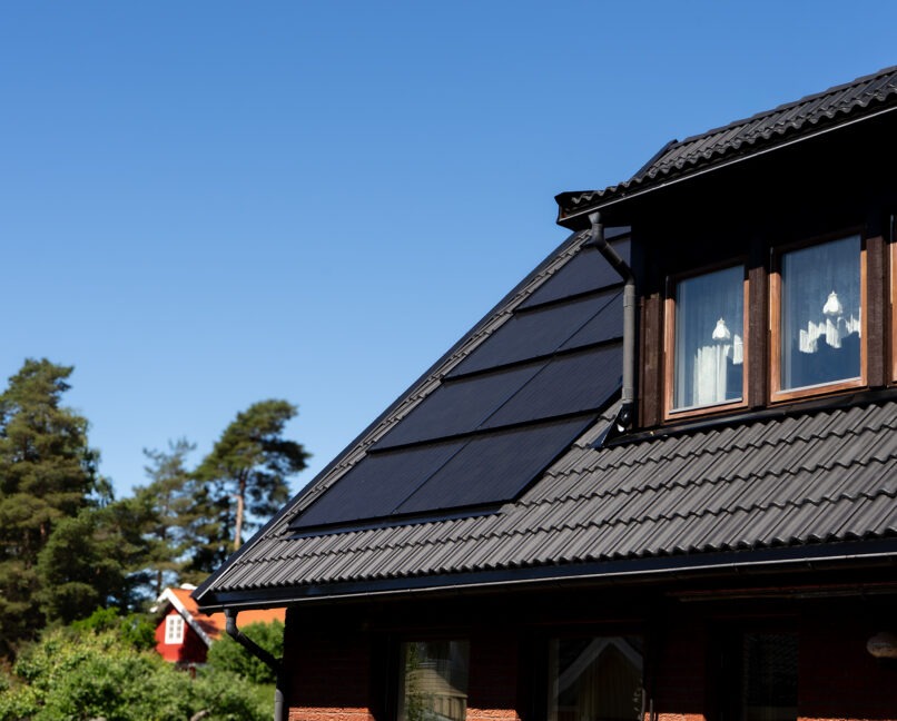 Svart betongtak med integrerade solceller på tegelhus.