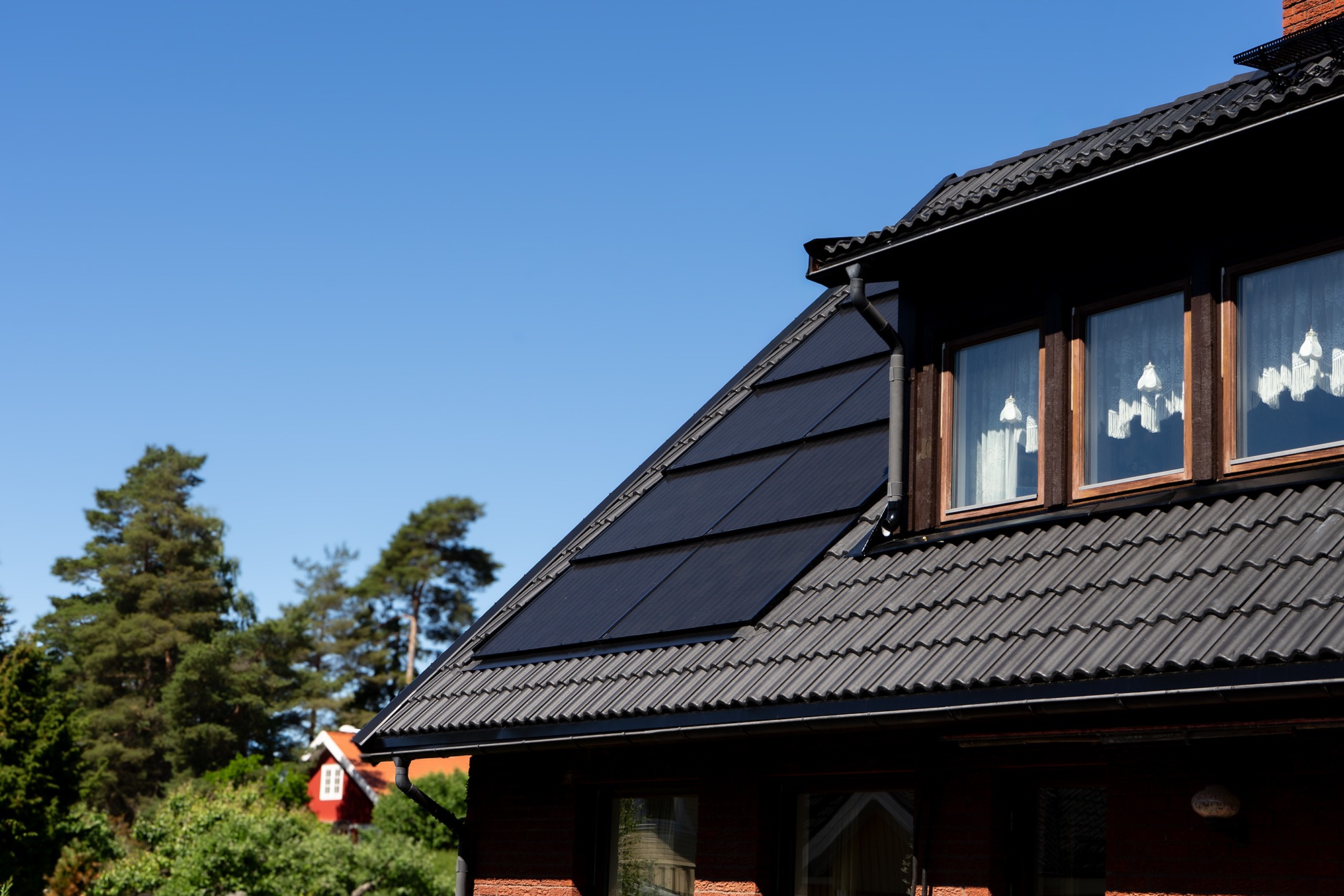 Svart betongtak med integrerade solceller på tegelhus.